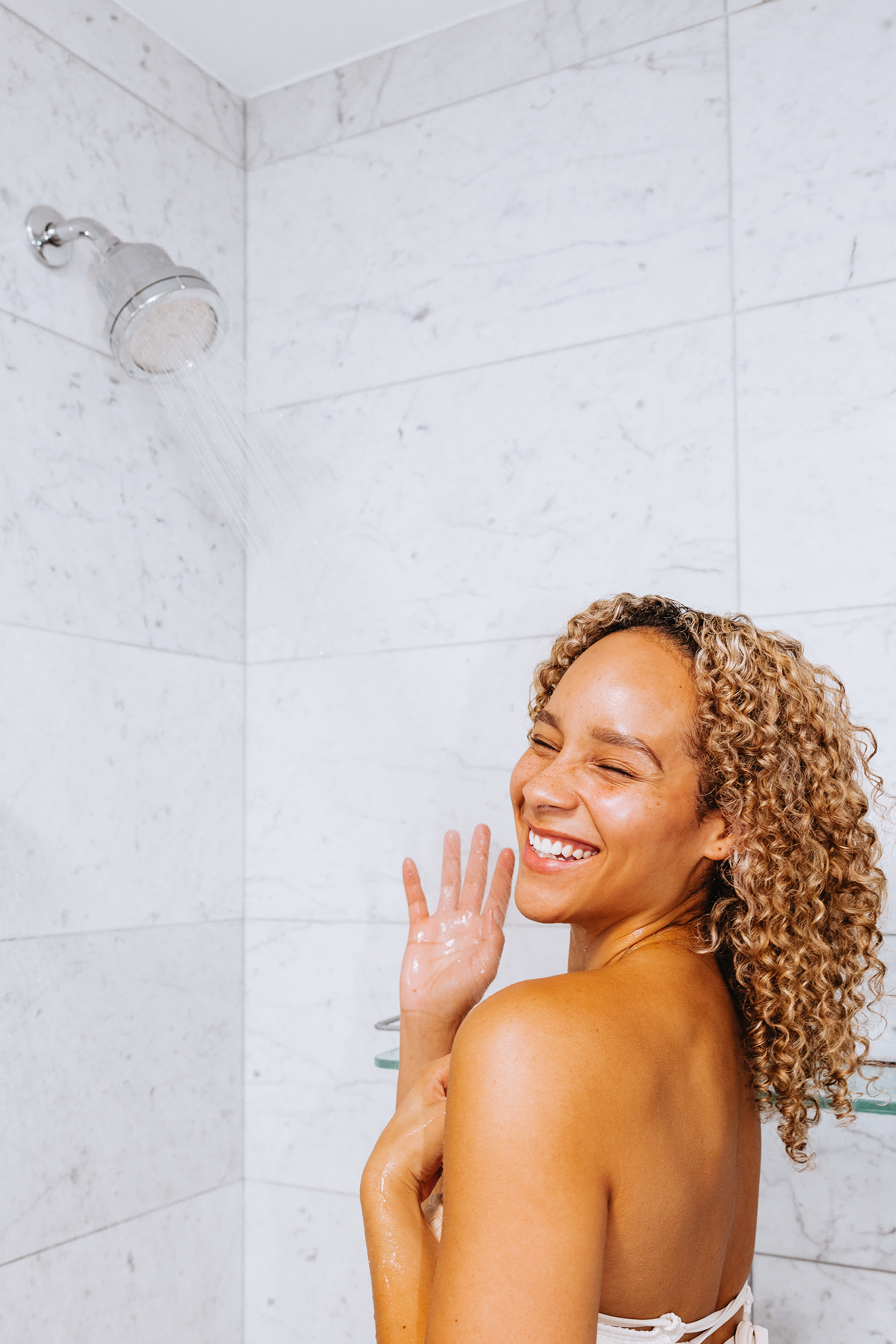 Person smiling while taking a shower under a chrome showerhead.