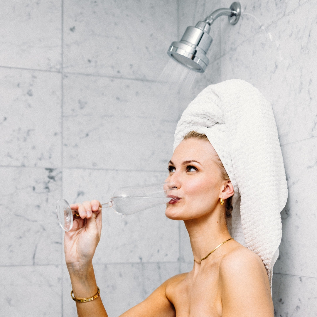 Person with towel drinking champagne in a shower.