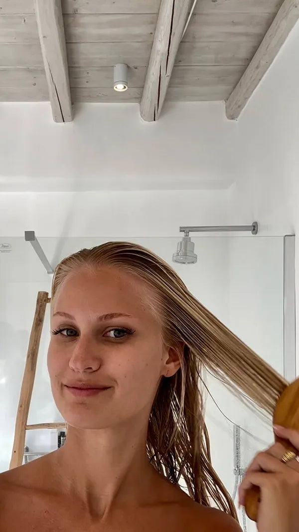 Person brushing their wet hair in a modern bathroom with wooden ceiling beams.